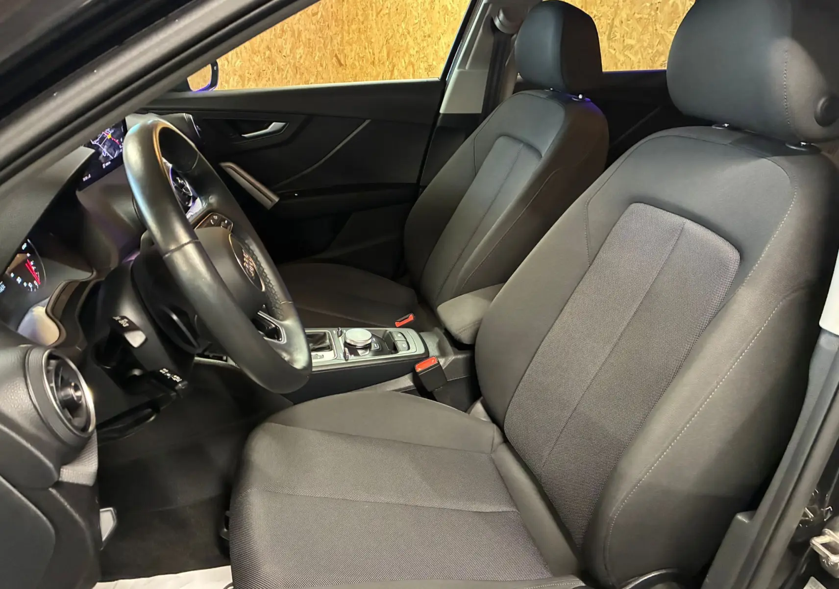 Vue intérieure côté conducteur de l'Audi Q2 35 TFSI S-Line 2023 avec sièges tissu noir et volant multifonction.