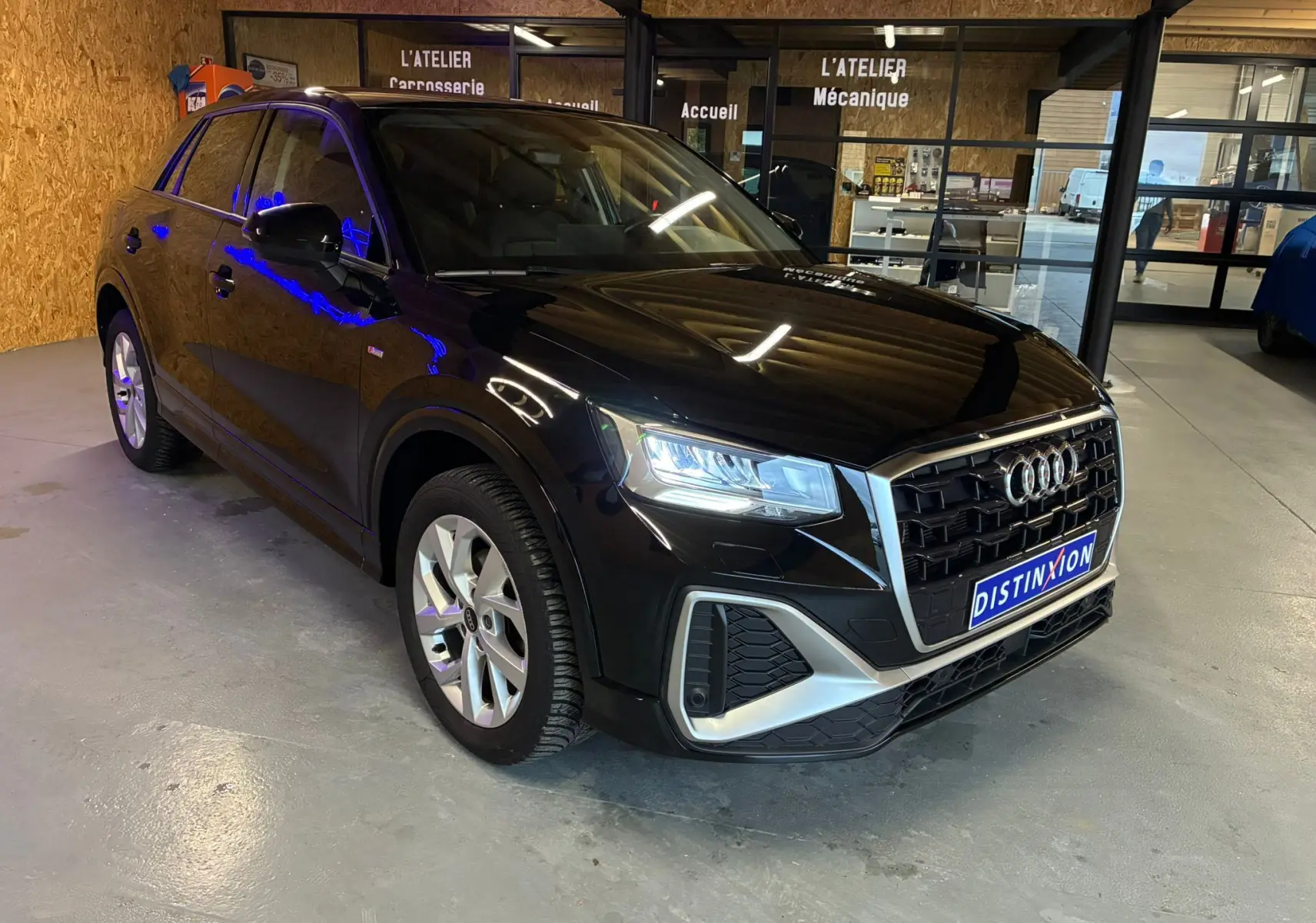 Audi Q2 35 TFSI S-Line noir vue 3/4 avant droit dans un garage avec phares allumés et calandre chromée.