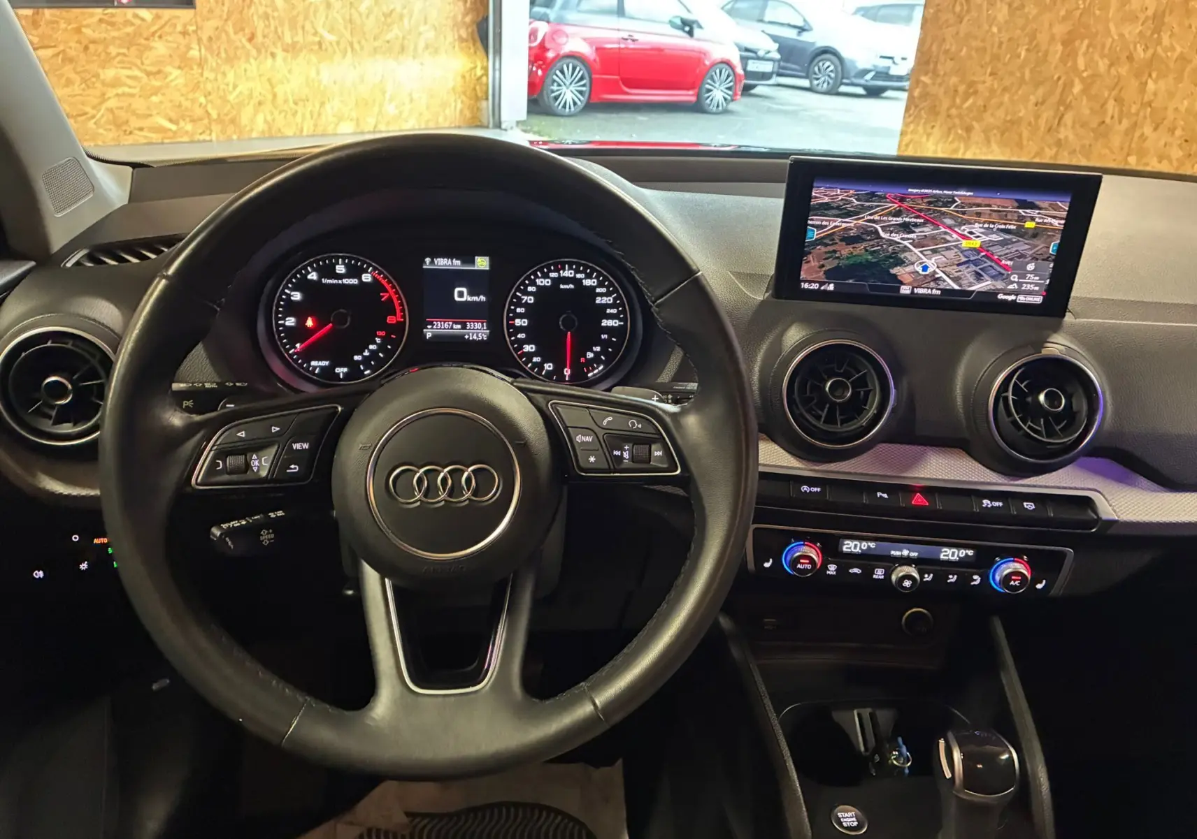 Tableau de bord noir de l'Audi Q2 35 TFSI 2023 avec écran GPS, commandes clim et volant multifonction côté gauche.
