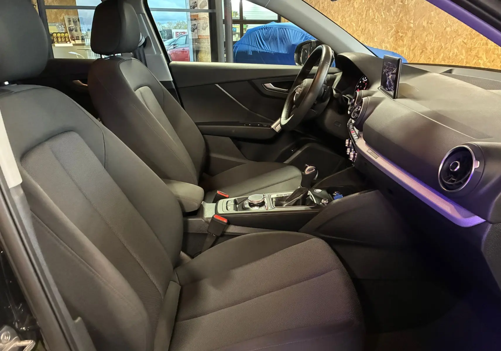 Intérieur noir de l'Audi Q2 35 TFSI 2023 vu côté conducteur, avec tableau de bord moderne et écran central déployé.