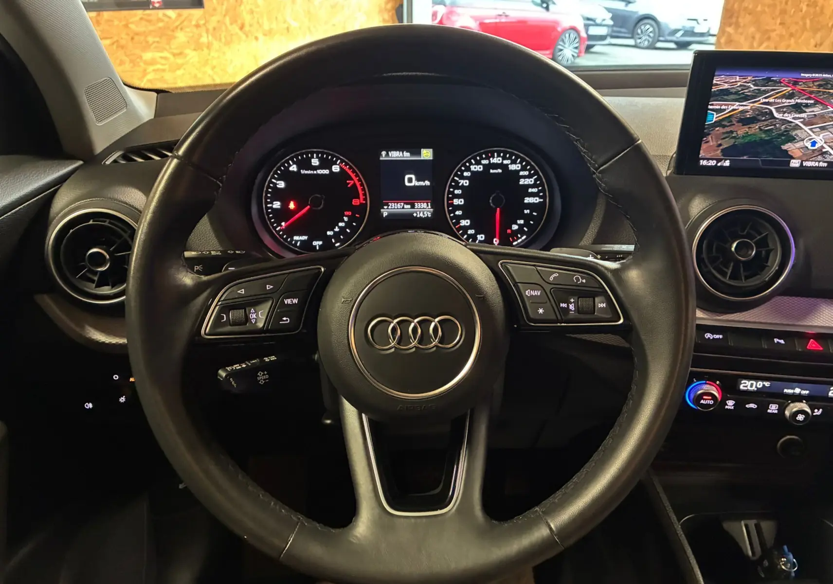 Vue intérieure centrée sur le volant cuir Audi d'un Q2 35 TFSI noir, avec tableau de bord digital et écran GPS à droite.