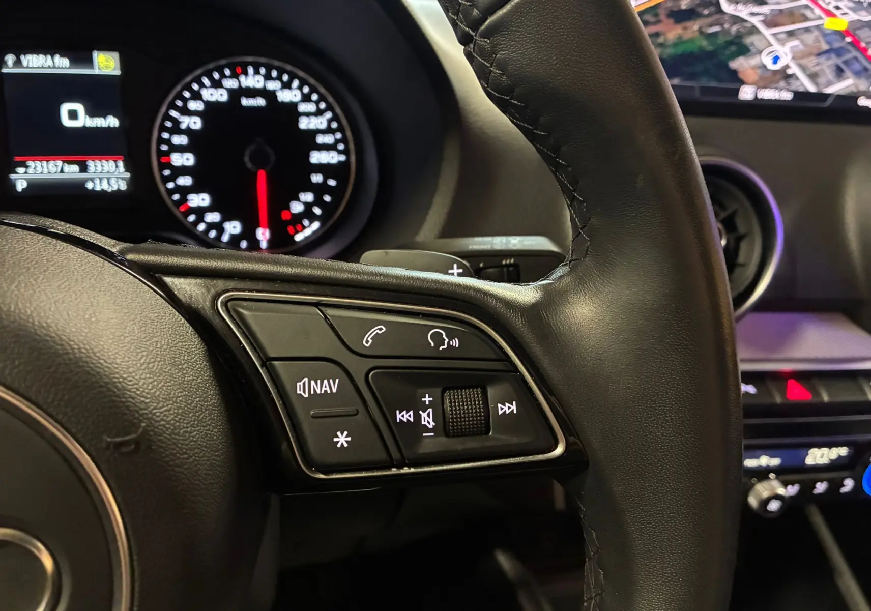 Gros plan sur le volant noir de l'Audi Q2 35 TFSI 2023, avec commandes audio et tableau de bord éclairé en arrière-plan.