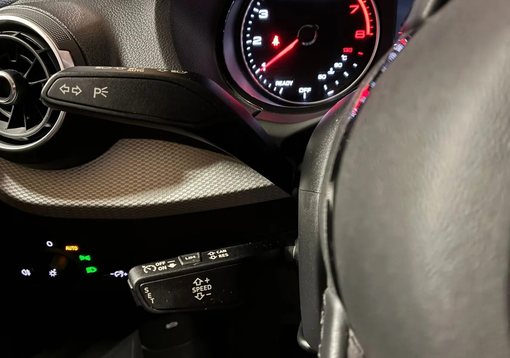 Détail intérieur du volant et des commandes au volant d'un Audi Q2 noir 2023, avec tableau de bord éclairé en rouge.