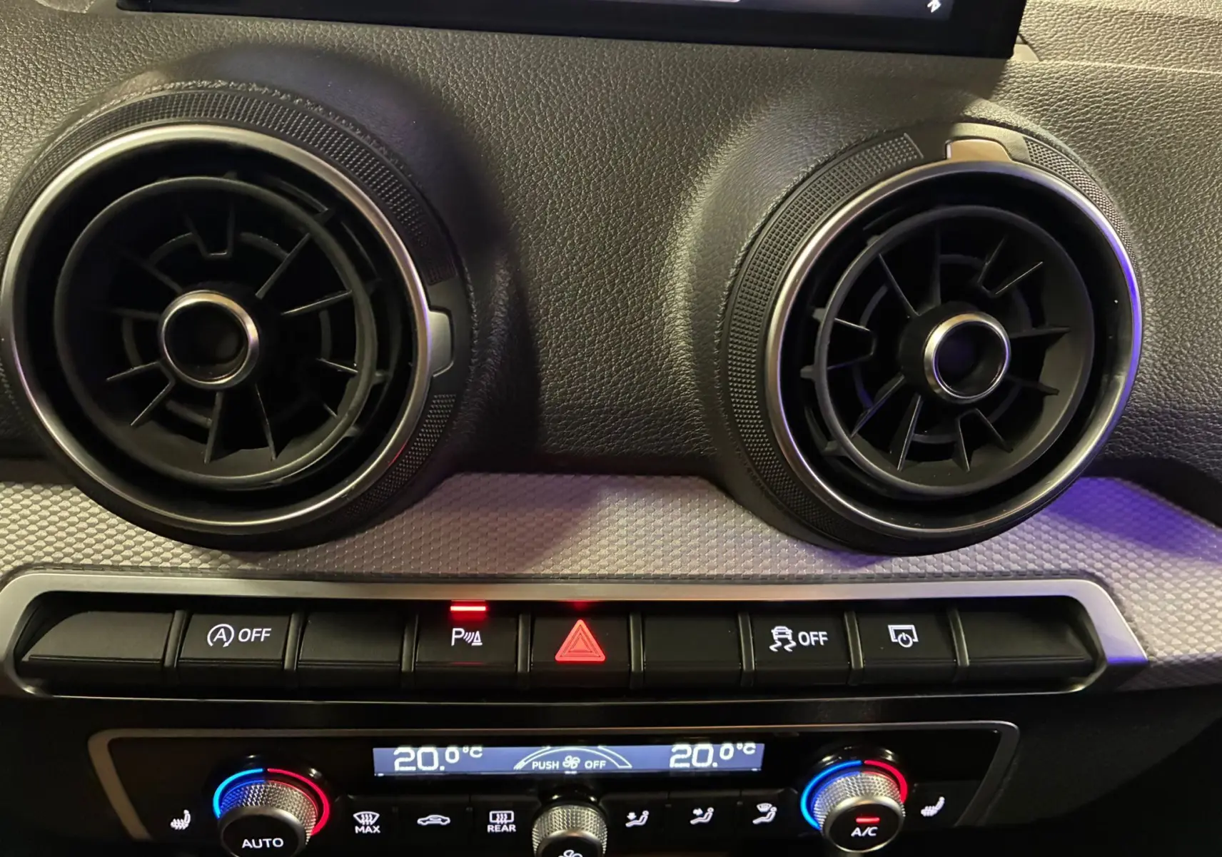 Détail du tableau de bord noir de l'Audi Q2 2023 avec aérateurs ronds et commandes de climatisation digitales.