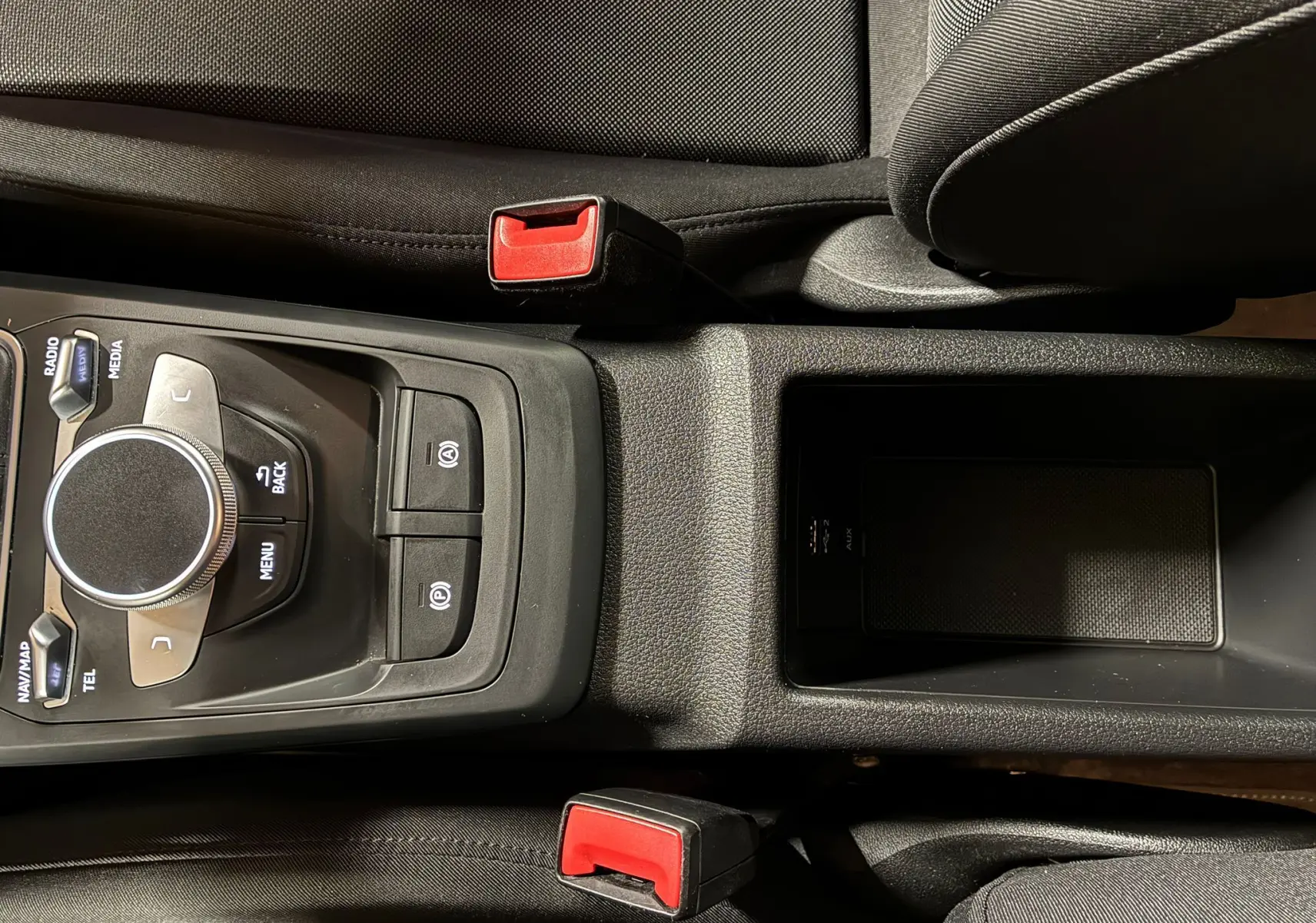 Vue rapprochée de la console centrale noire de l'Audi Q2 35 TFSI S-Line 2023 avec commandes multimédia et ceintures rouges.