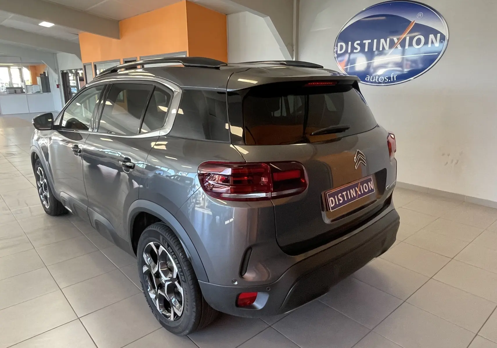 Vue 3/4 arrière droite du Citroën C5 Aircross hybride gris platinium avec jantes alliage biton et barres de toit.