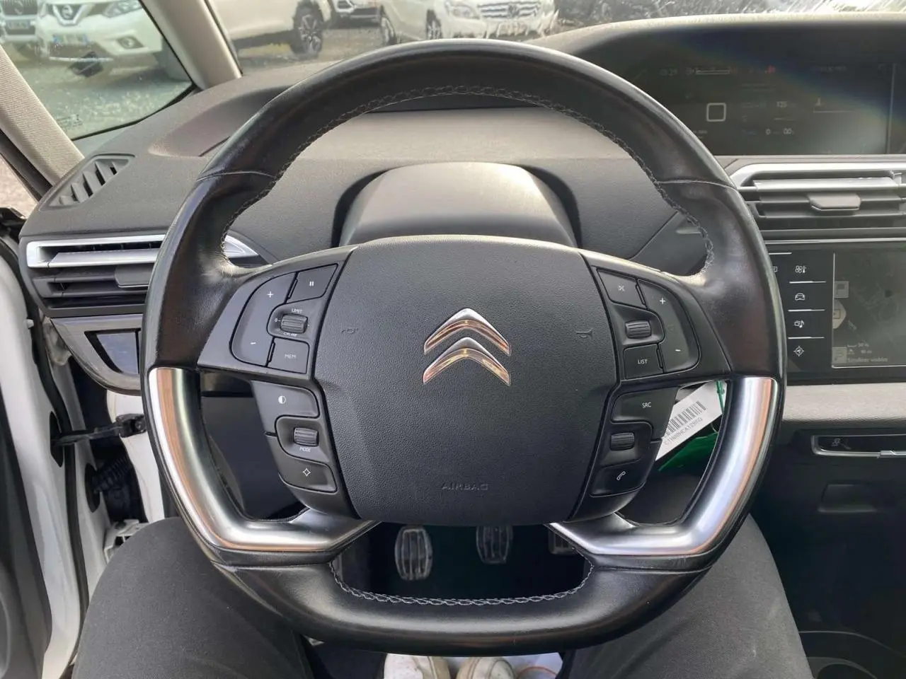 Vue centrée sur le volant cuir noir du Citroën Grand C4 Picasso blanc, avec commandes intégrées et tableau de bord numérique.