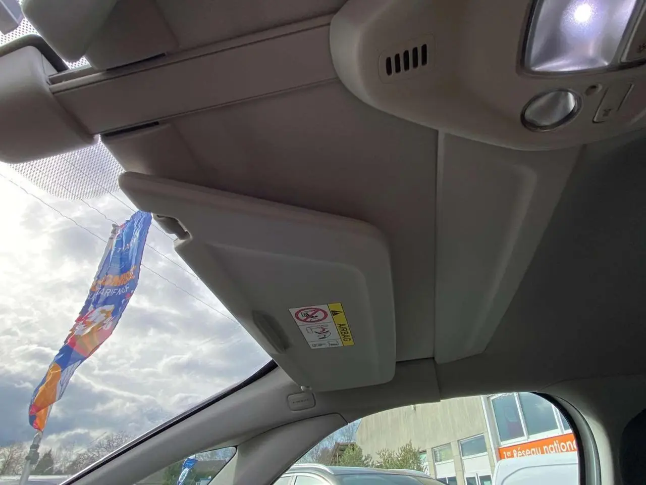 Intérieur du Citroën Grand C4 Picasso 2015, vue du pare-soleil conducteur beige avec ciel nuageux visible.