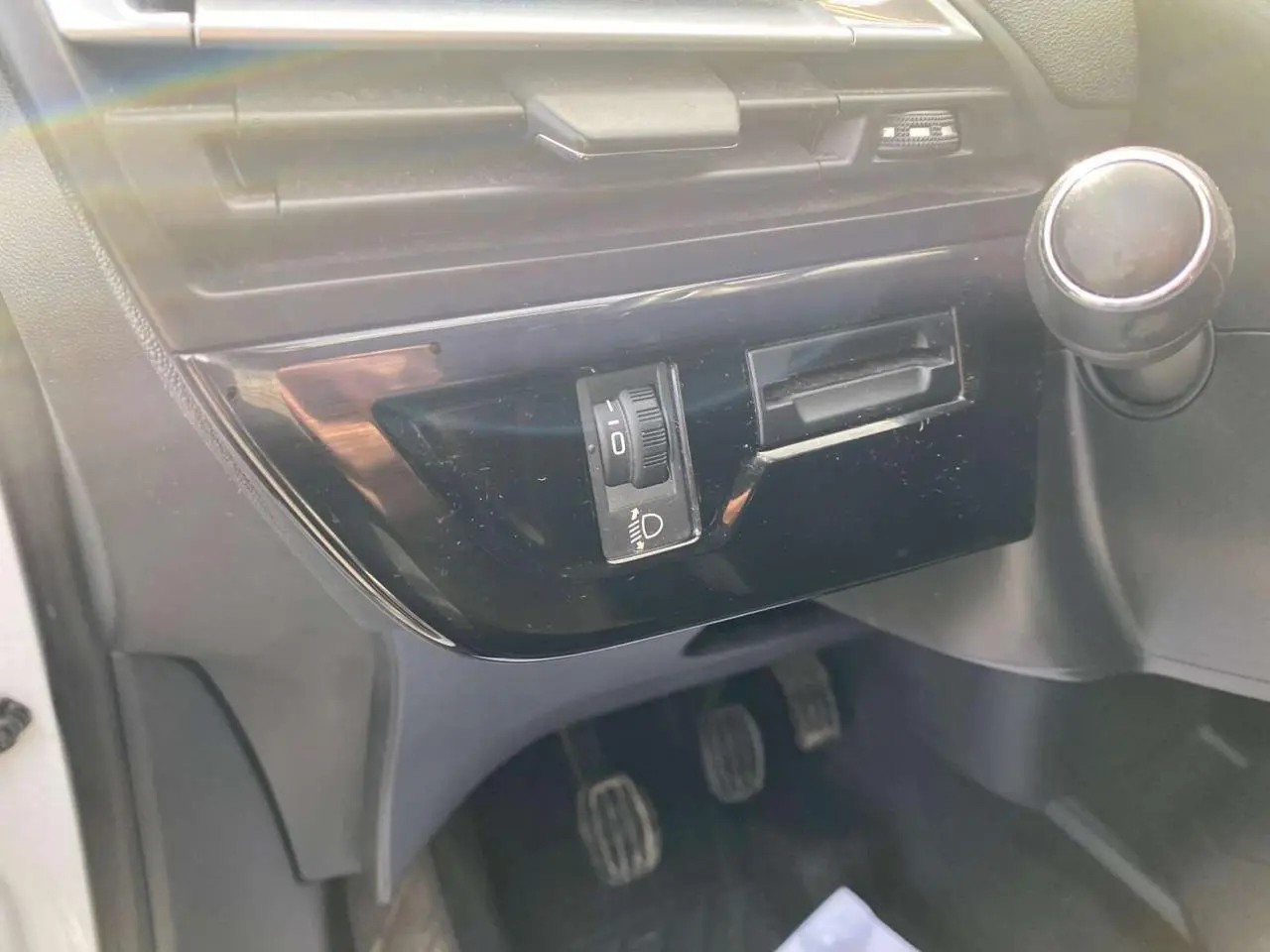 Détail intérieur côté conducteur du tableau de bord du Citroën Grand C4 Picasso blanc, avec commande de réglage des phares et levier de boîte manuelle.