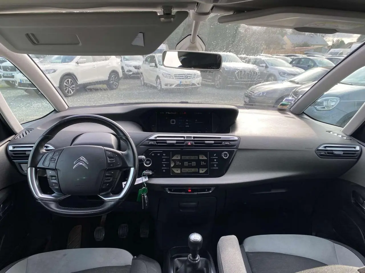 Vue intérieure frontale du tableau de bord et volant cuir noir du Citroën Grand C4 Picasso blanc, avec écran tactile et boîte manuelle.