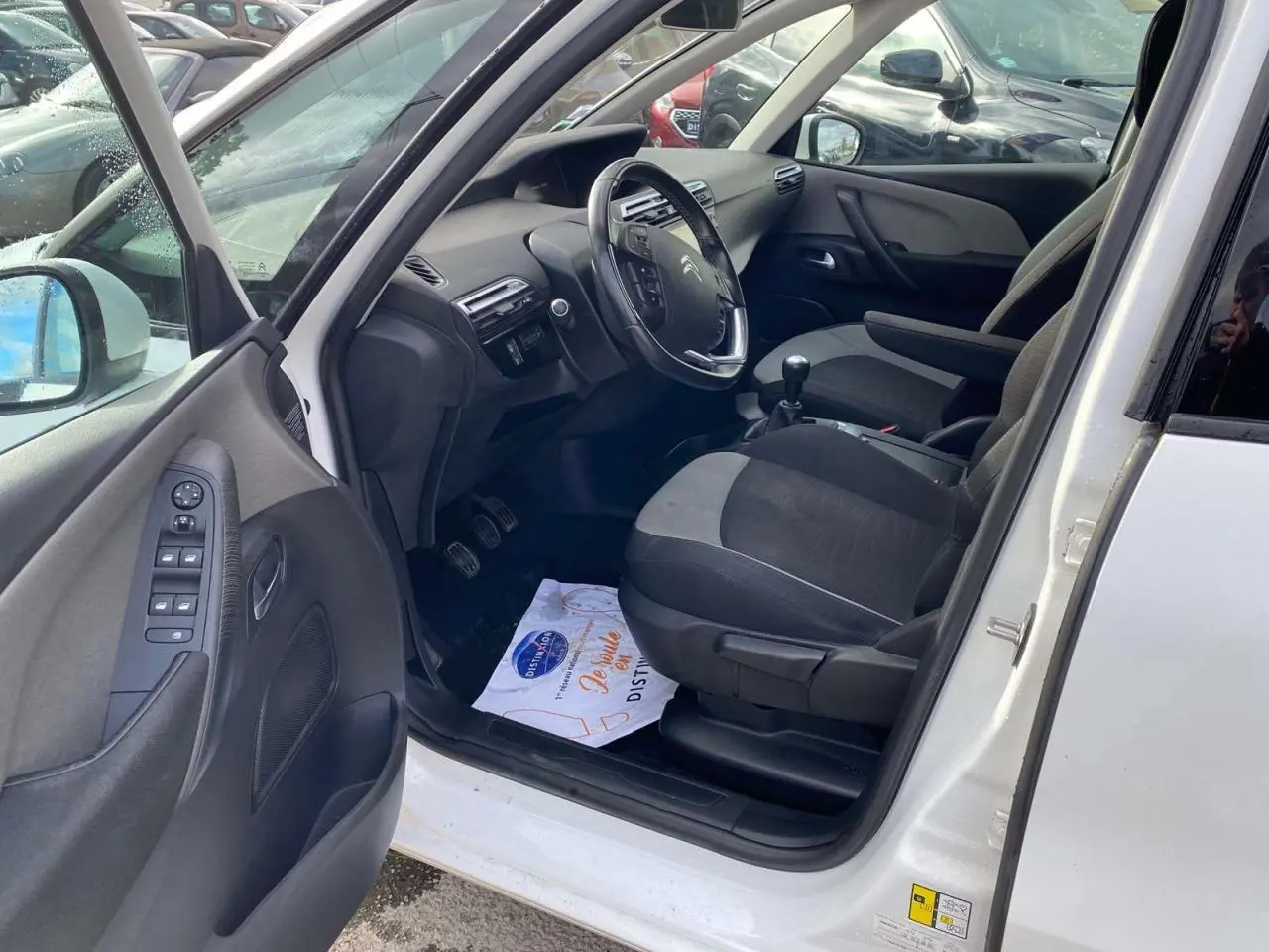 Vue intérieure côté conducteur d'un Citroën Grand C4 Picasso blanc, montrant sièges tissu bicolore et volant multifonction.