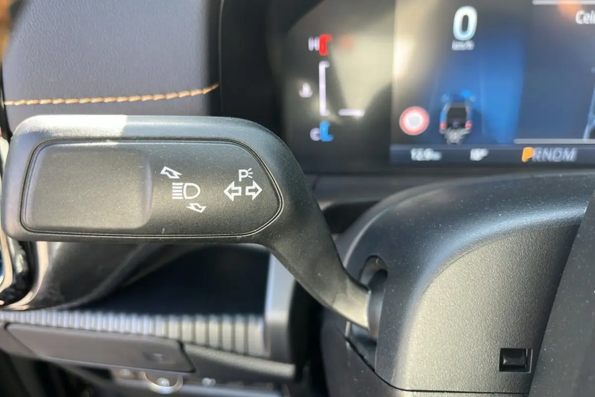 Gros plan sur la commande de clignotants et feux du Ford Ranger PHEV 281 Wildtrak gris carbone, tableau de bord en arrière-plan.