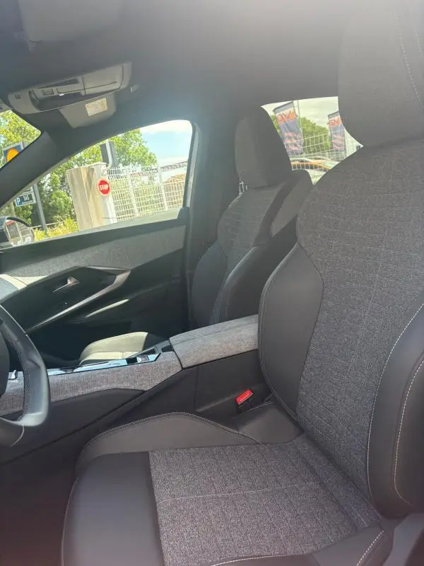 Vue intérieure côté conducteur du Peugeot 3008 Hybrid 136 e-DCS6 Allure 2025, sièges gris tissu et cuir avec console centrale assortie.