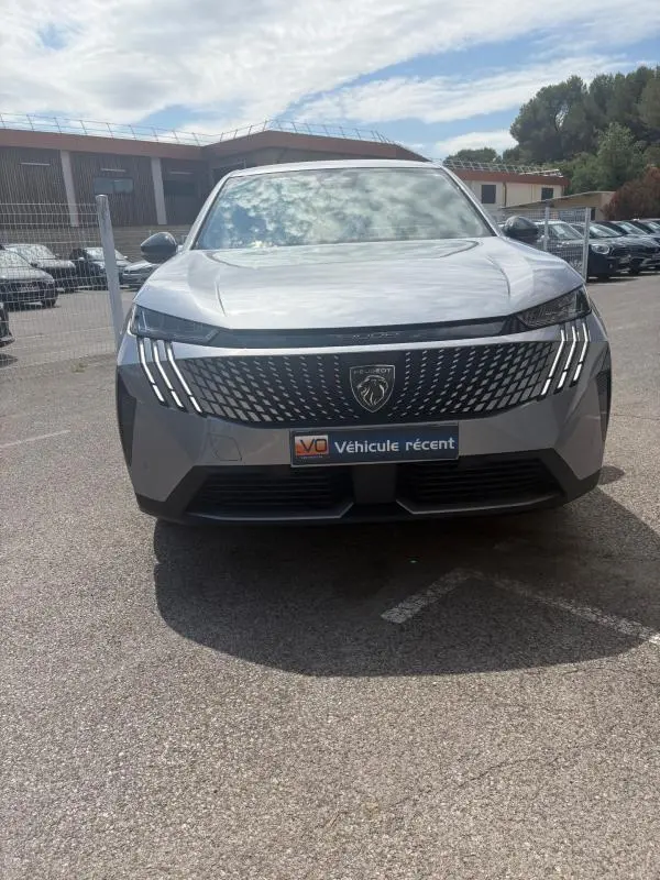Vue frontale d'un Peugeot 3008 Hybrid gris clair 2025 avec calandre noire et feux LED distinctifs en forme de griffes.