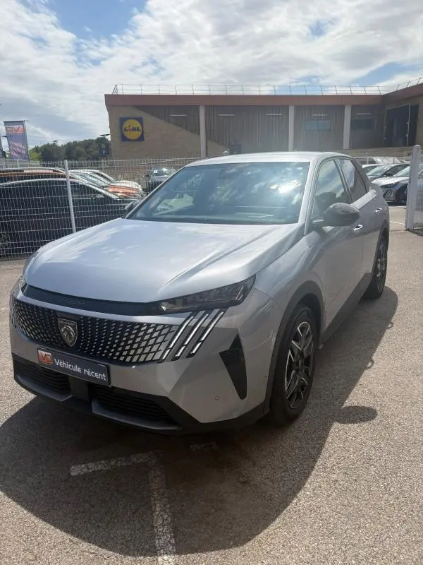 Vue 3/4 avant d'un Peugeot 3008 Hybrid gris clair 2025 avec calandre distinctive et feux LED verticaux.