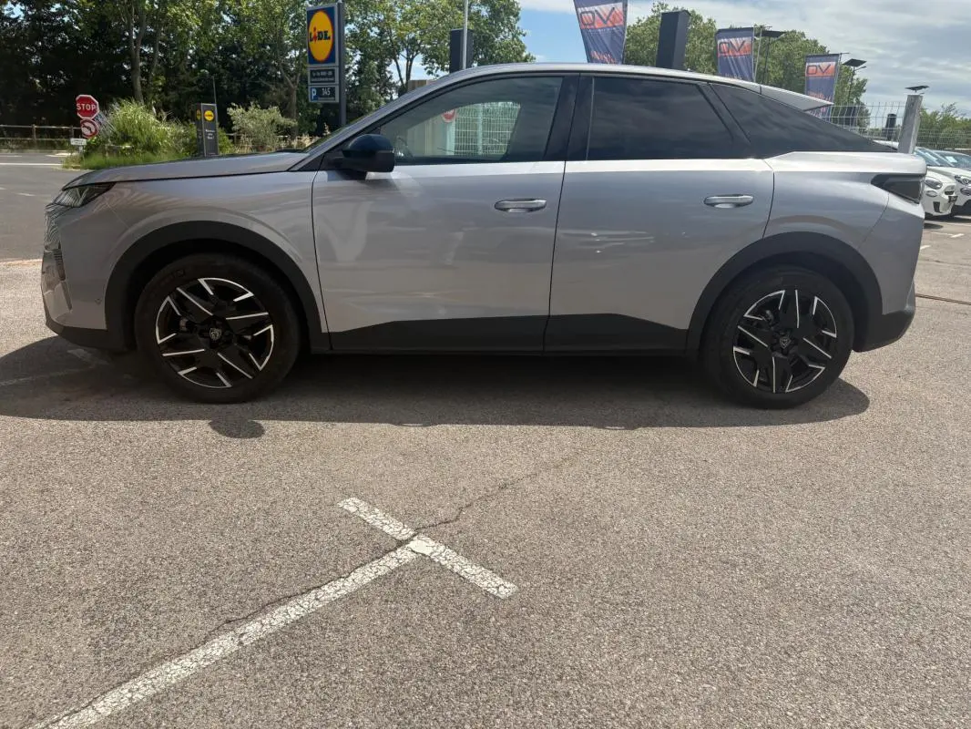 Vue de profil côté gauche d’un Peugeot 3008 Hybrid gris clair 2025 avec jantes noires au design moderne.