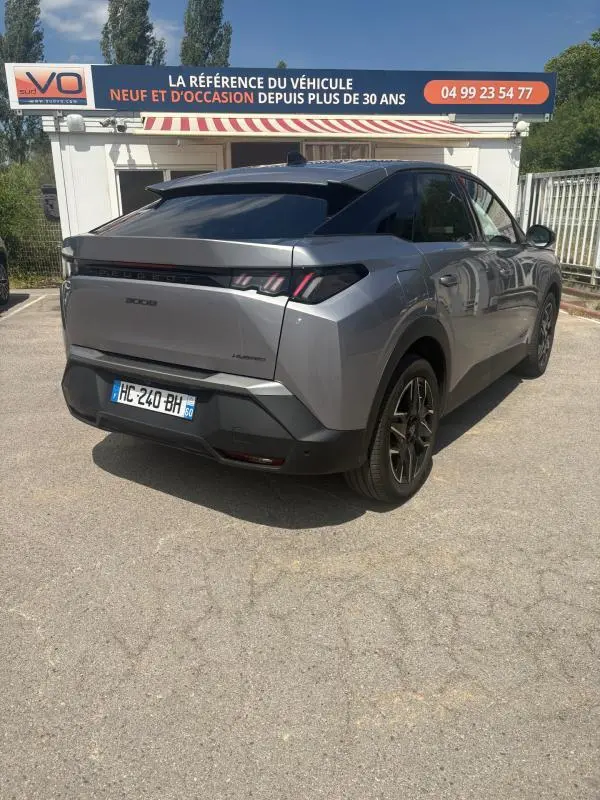 Vue 3/4 arrière droite d’un Peugeot 3008 Hybrid gris clair 2025 avec feux arrière distinctifs et toit noir.