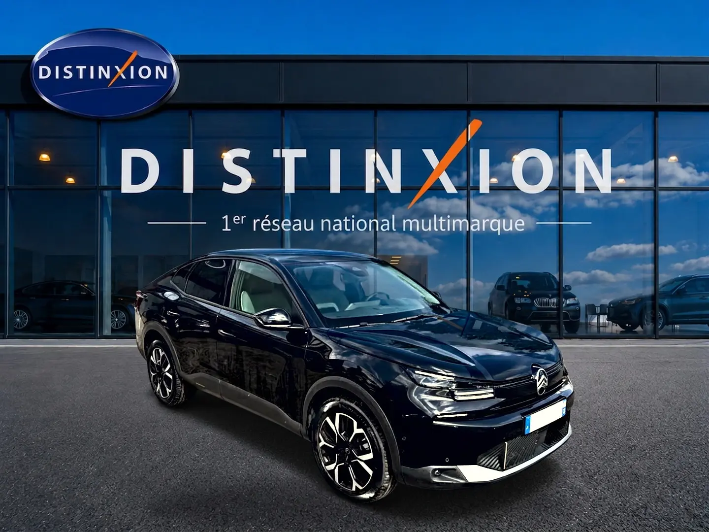 Citroën C4 X noir vue 3/4 avant droit, jantes alu noires et calandre distinctive sous un ciel bleu.
