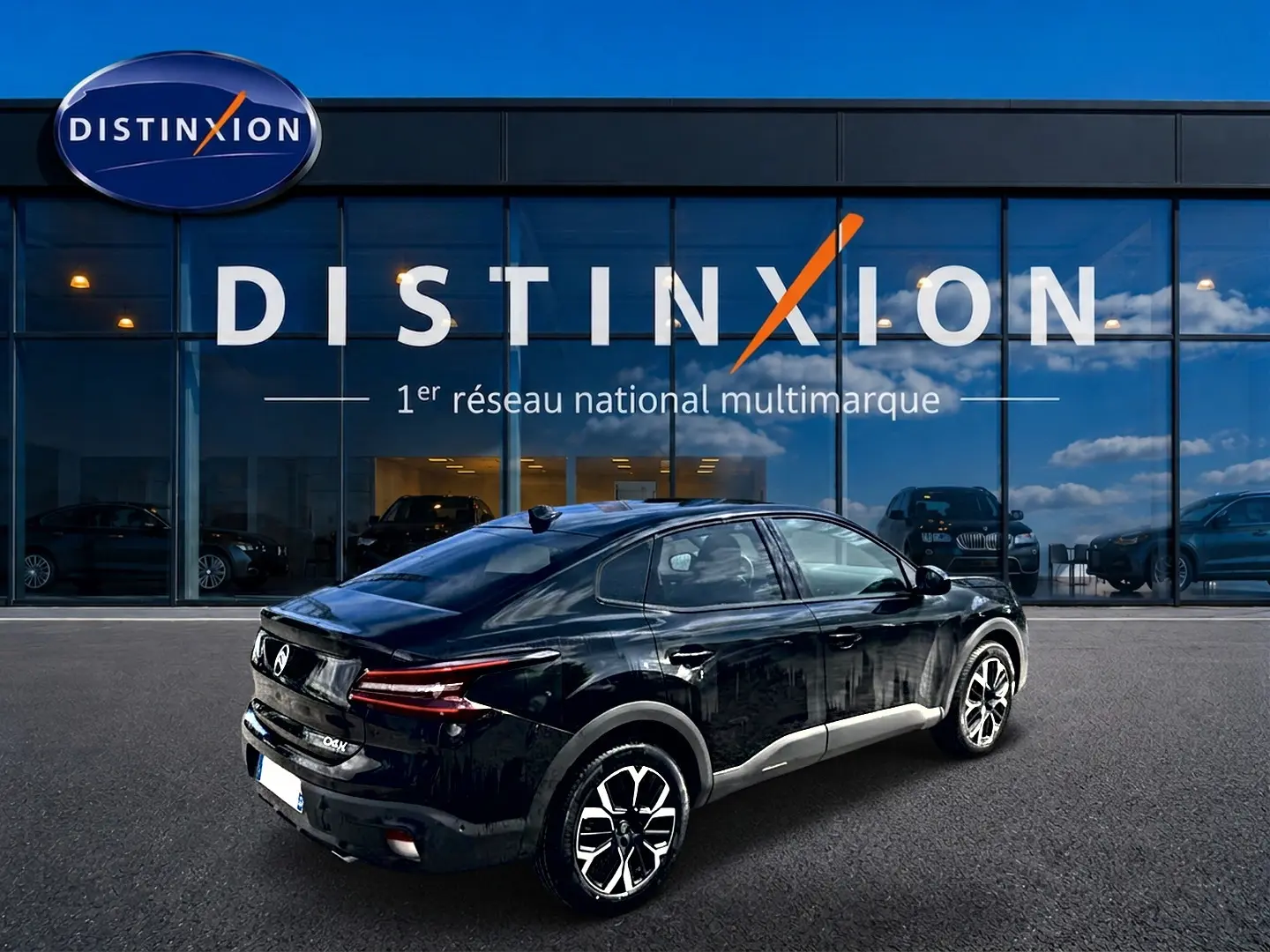 Vue 3/4 arrière droite d'une Citroën C4 X noire 2025 avec jantes alu et feux arrière LED devant un showroom Distinxion.