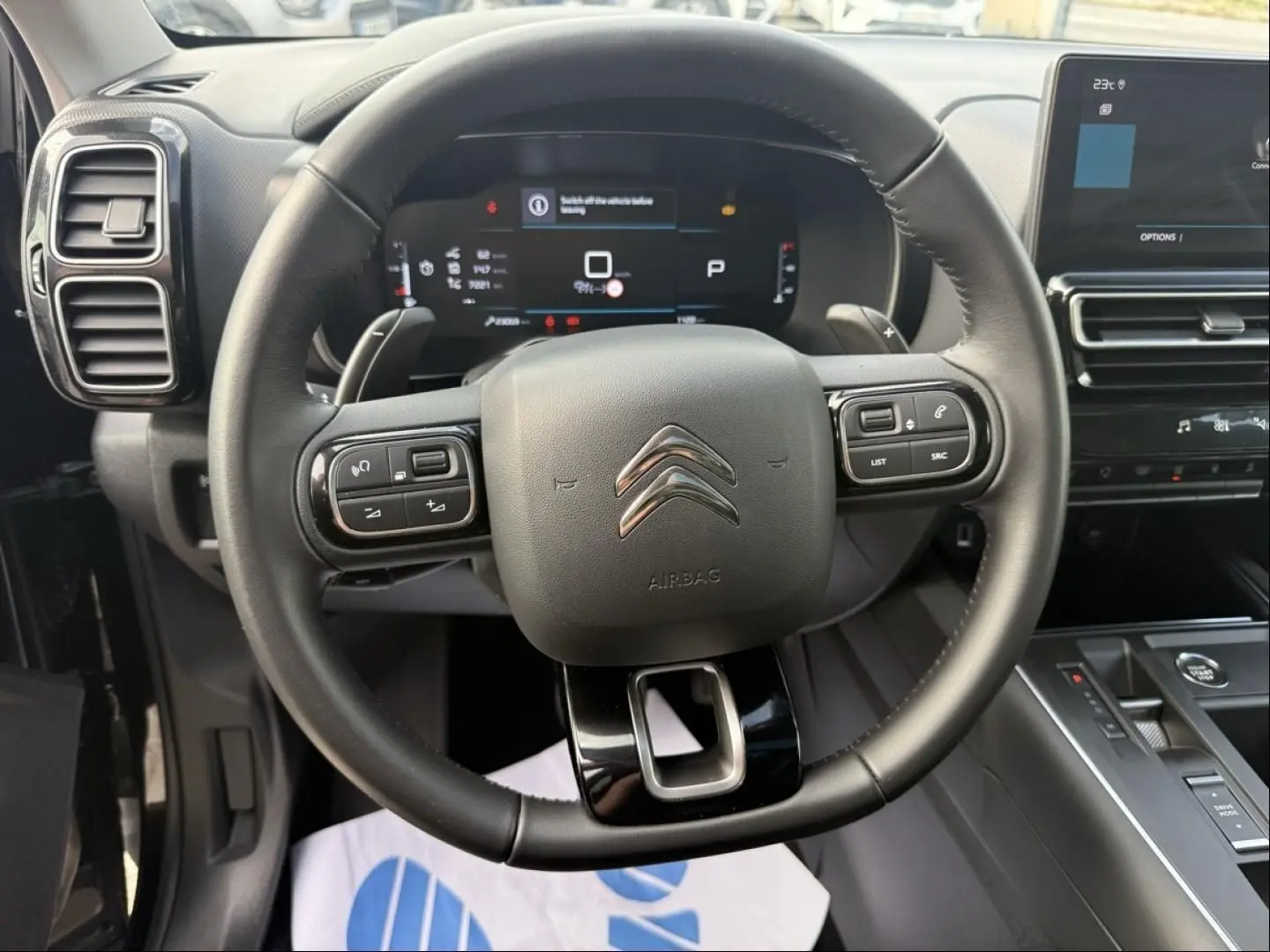 Vue intérieure centrée sur le volant noir du Citroën C5 Aircross 2024 avec tableau de bord numérique et console moderne.