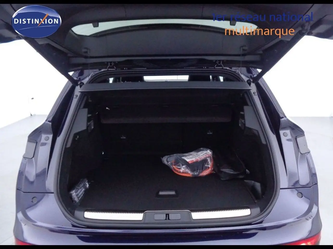 Coffre ouvert vu de l'arrière d'un DS7 Crossback hybride bleu encre métal avec intérieur de coffre noir et accessoires.