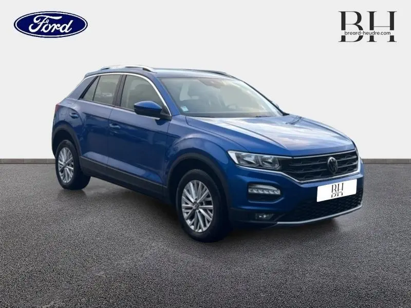 Volkswagen T-Roc bleu Ravenna métallisé vu en 3/4 avant droit avec jantes alu et barres de toit.