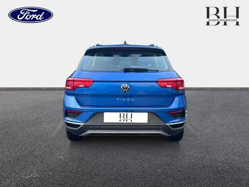 Vue arrière d'un Volkswagen T-Roc bleu Ravenna métallisé avec feux arrière LED et becquet noir.