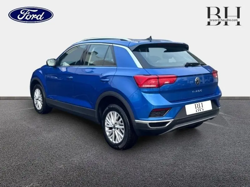 Vue 3/4 arrière droite d'un Volkswagen T-Roc bleu Ravenna métallisé avec barres de toit et jantes alu.