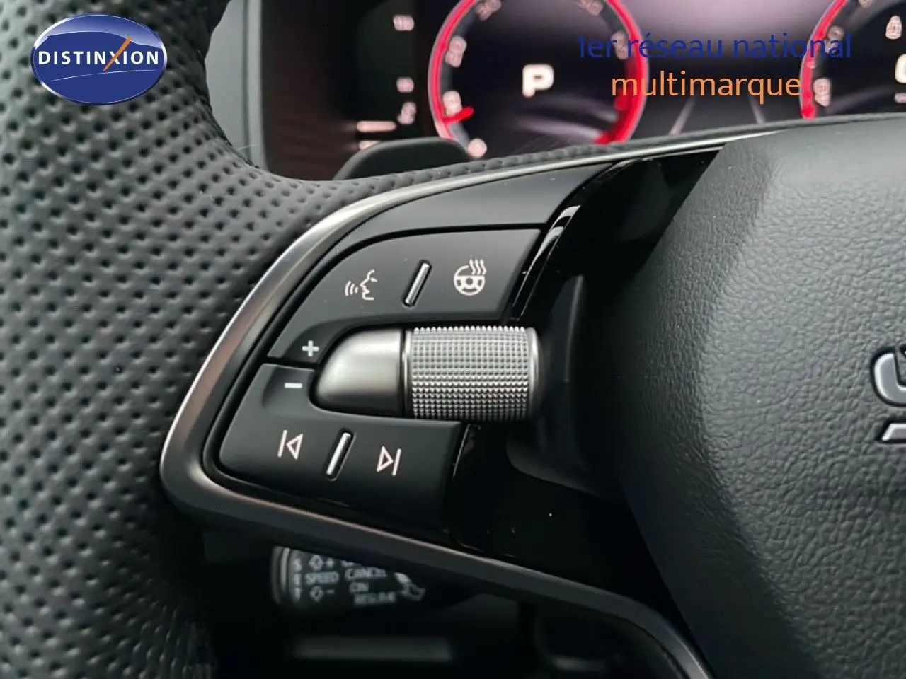 Gros plan sur les commandes au volant perforé d’un Skoda Karoq 1.5 TSI, avec tableau de bord numérique en arrière-plan.