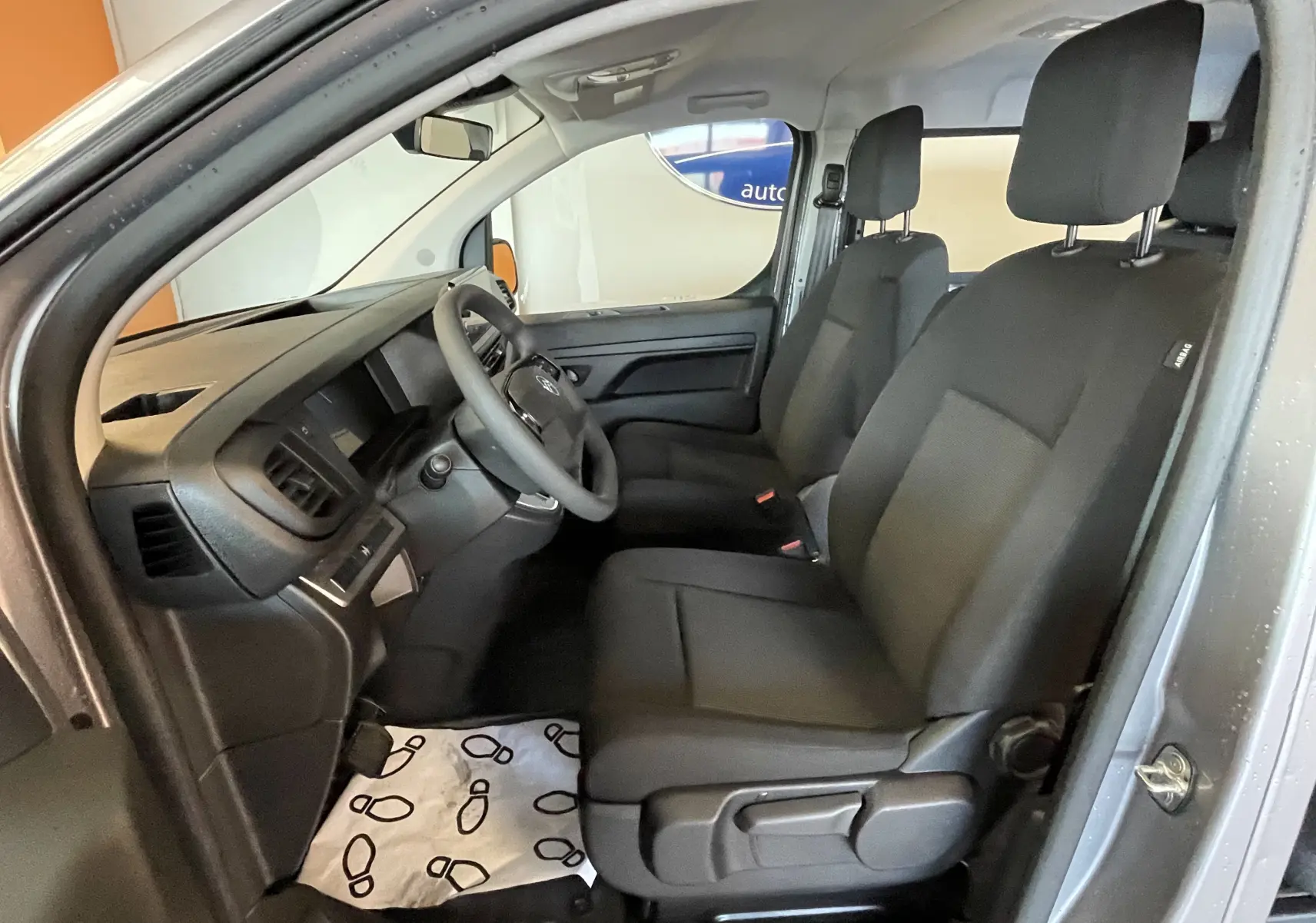 Vue intérieure côté conducteur du Citroën Jumpy gris Artense, montrant les sièges noirs et le tableau de bord épuré.