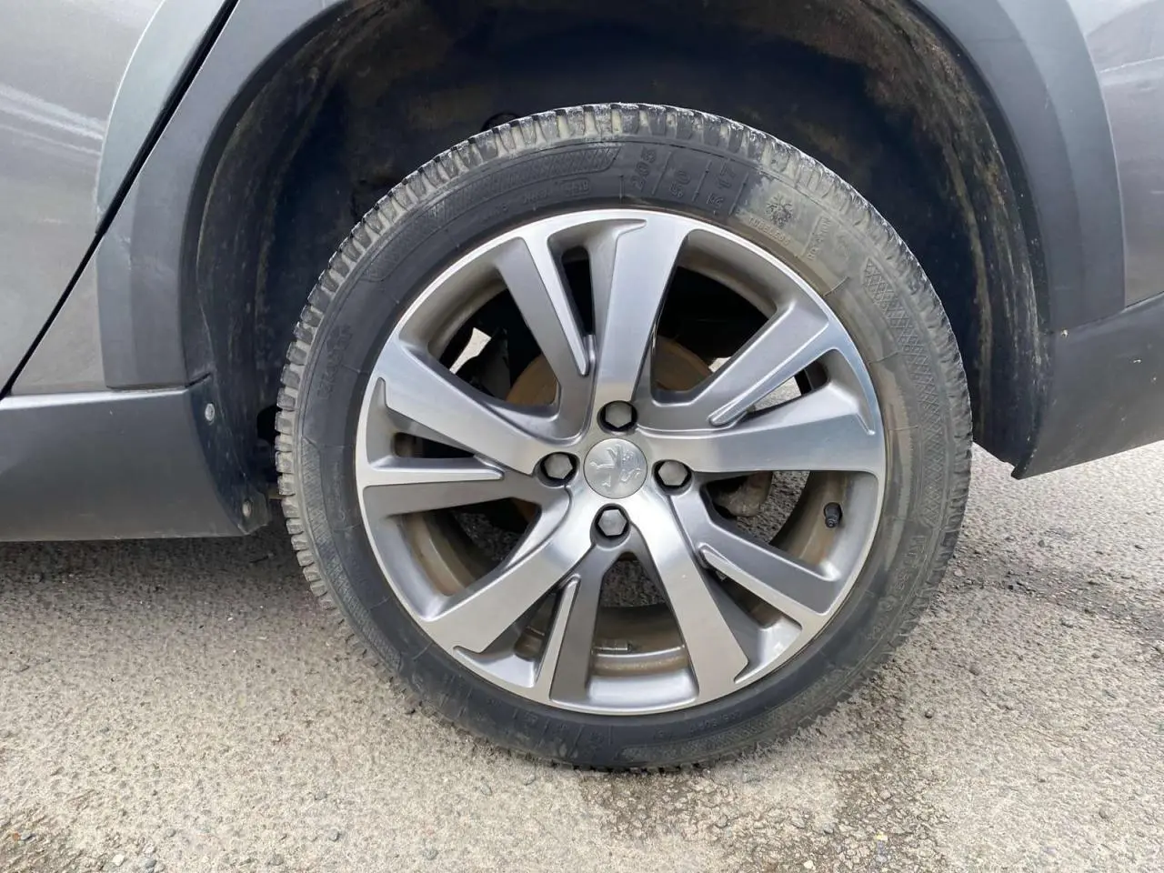 Gros plan sur la roue avant droite d’un Peugeot 2008 gris platinium, mettant en valeur la jante alliage à cinq doubles branches.