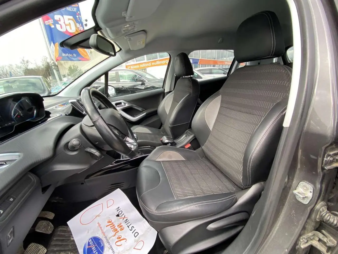 Vue intérieure côté conducteur de la Peugeot 2008 gris platinium, montrant sièges et volant noir avec tableau de bord moderne.