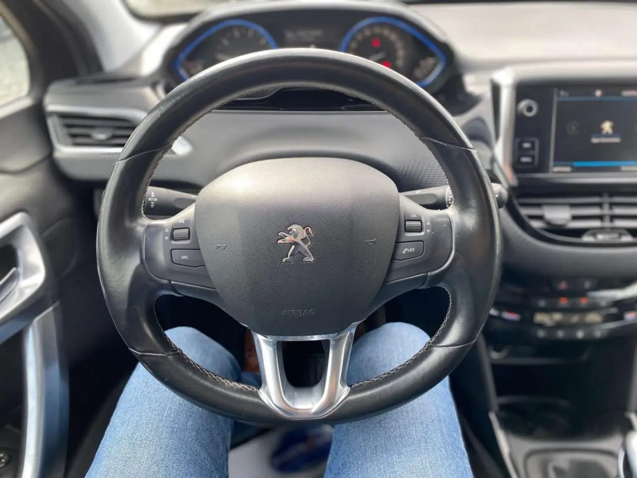 Vue intérieure centrée sur le volant cuir noir du Peugeot 2008 avec tableau de bord et écran tactile en arrière-plan.