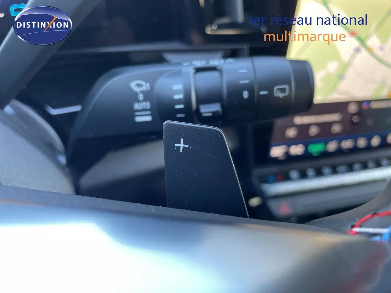 Gros plan sur la palette de changement de vitesse + au volant d’un Renault Austral noir étoile métal, avec tableau de bord numérique en arrière-plan.