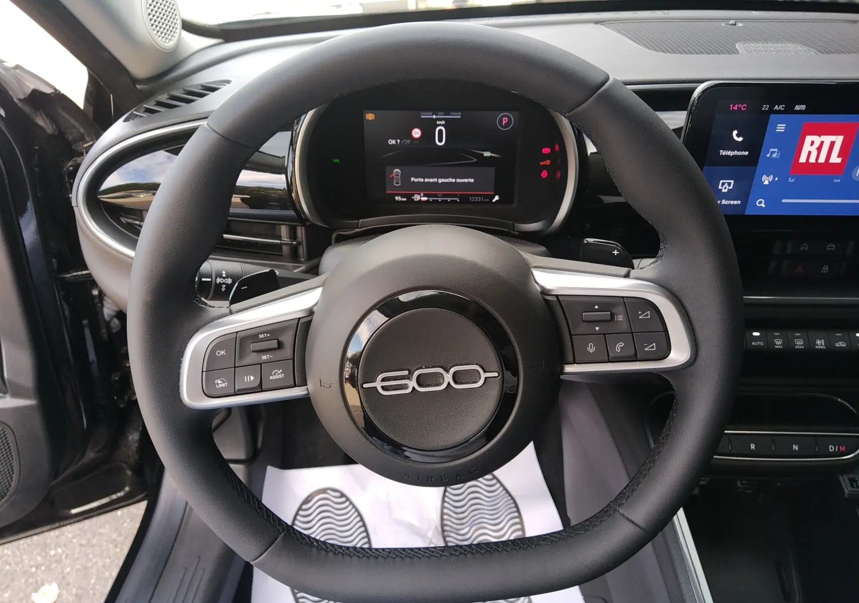 Vue intérieure centrée sur le volant noir du Fiat 600 2025 avec tableau de bord numérique et écran tactile RTL visible.
