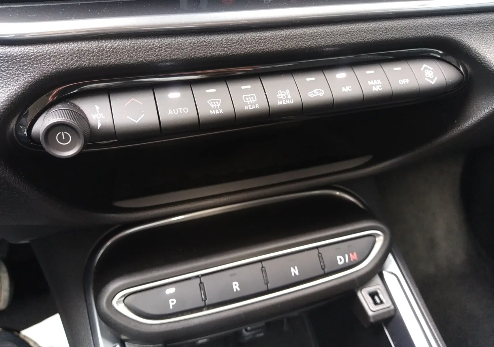 Vue rapprochée de la console centrale noire du Fiat 600 2025, montrant les commandes climatisation et la boîte auto à boutons.