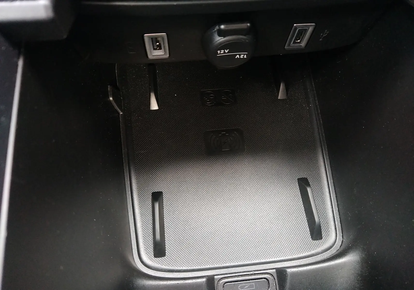 Vue rapprochée de la zone de recharge sans fil et ports USB dans l’habitacle noir de la FIAT 600 hybride 2025.