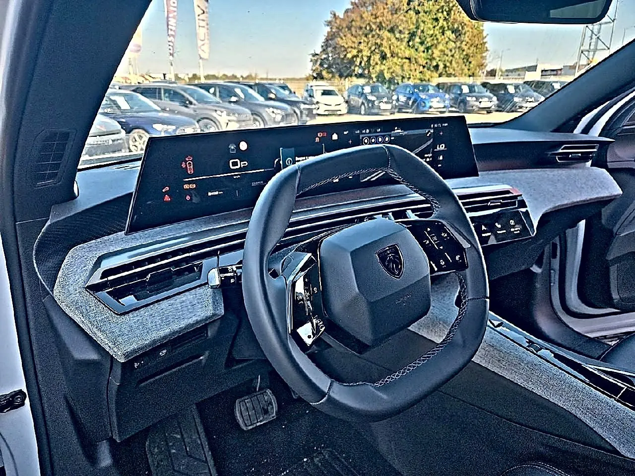 Vue intérieure côté conducteur du Peugeot 5008 blanc 2025, volant cuir et tableau de bord numérique large avec habillage tissu gris.