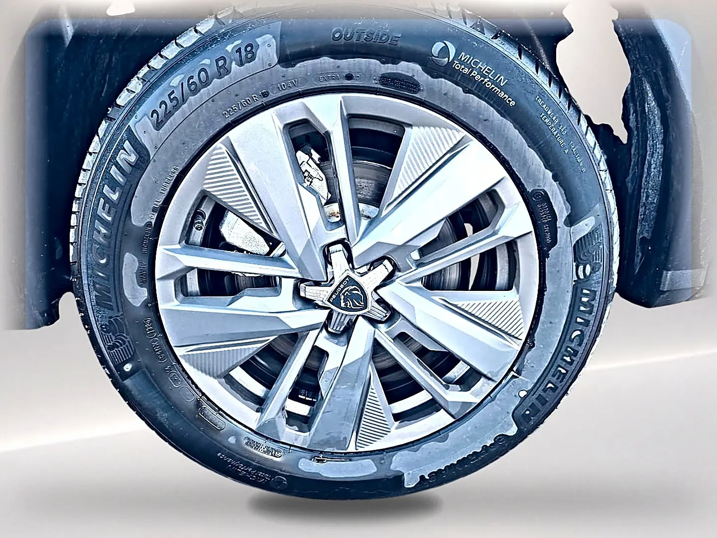 Gros plan sur la jante alu argentée Michelin d’un Peugeot 5008 blanc, mettant en valeur le logo lion au centre.