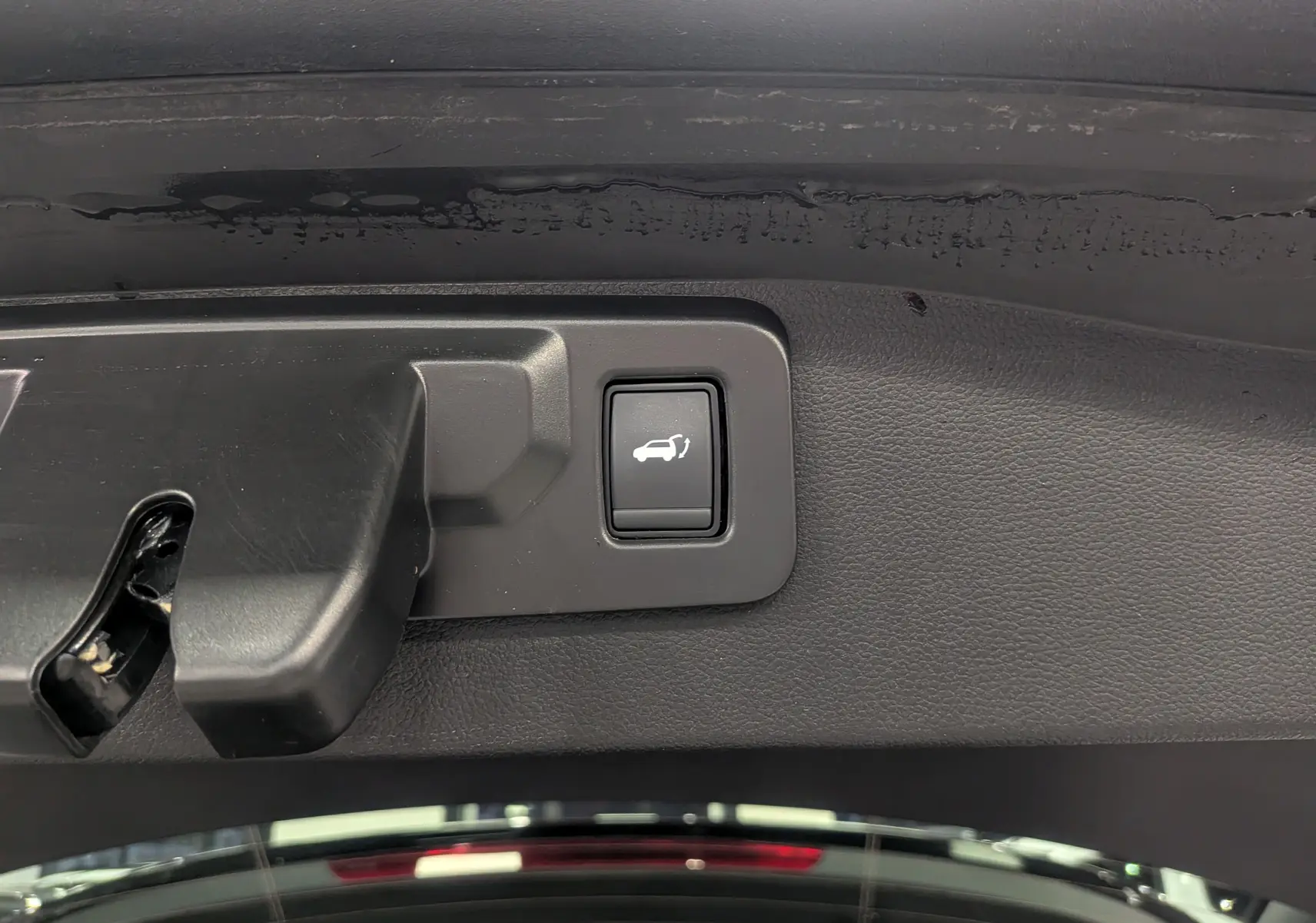 Bouton d'ouverture électrique du coffre sur la partie intérieure du hayon d'un Renault Austral gris Schiste toit noir.