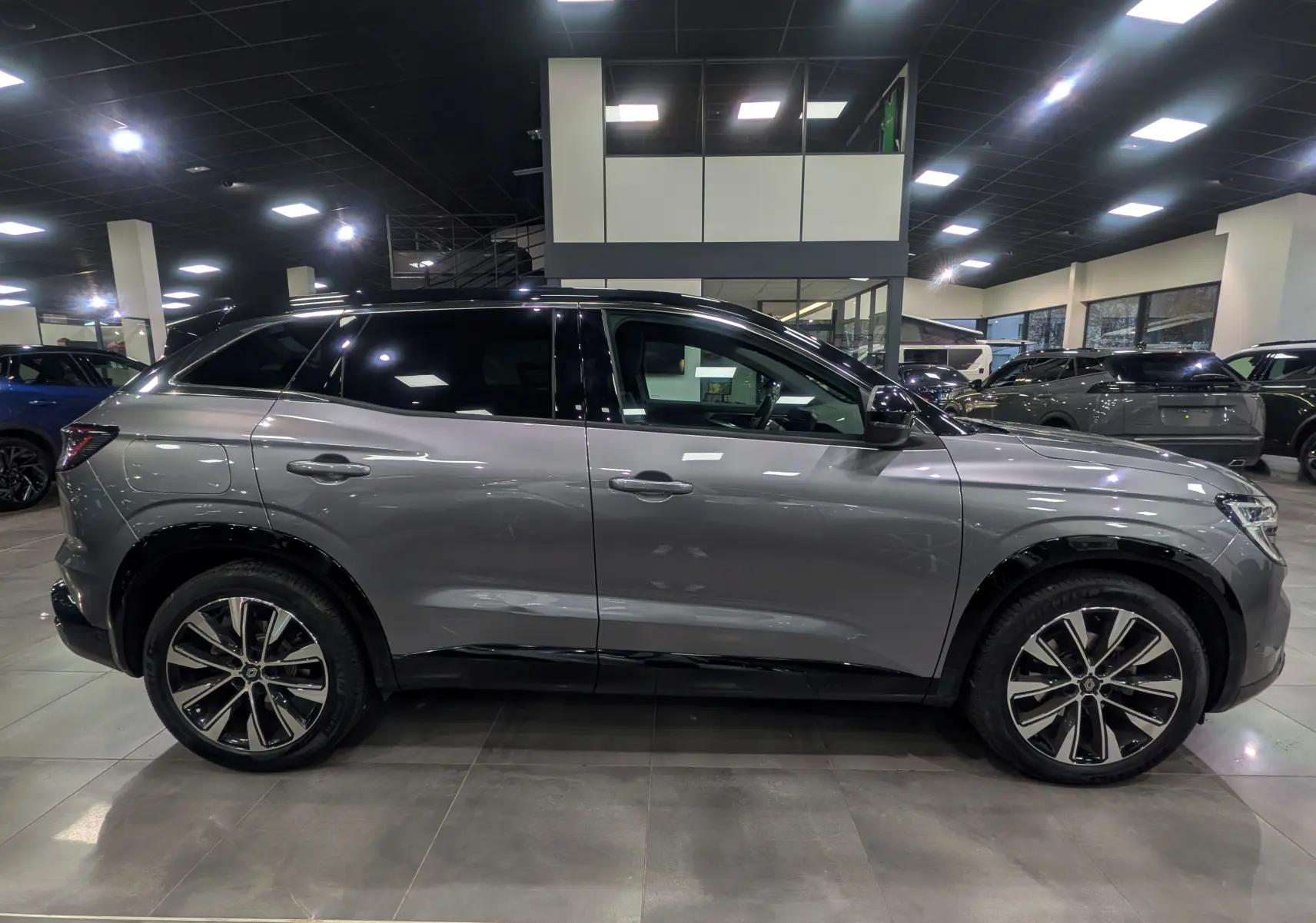 Vue latérale droite du Renault Austral 2024 gris schiste avec toit noir et jantes alliage bicolores en showroom.