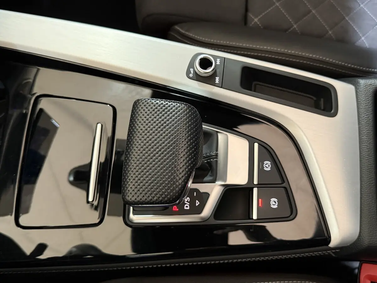 Vue rapprochée de la console centrale avec levier de vitesse noir texturé et finitions aluminium dans une Audi A4 gris foncé.