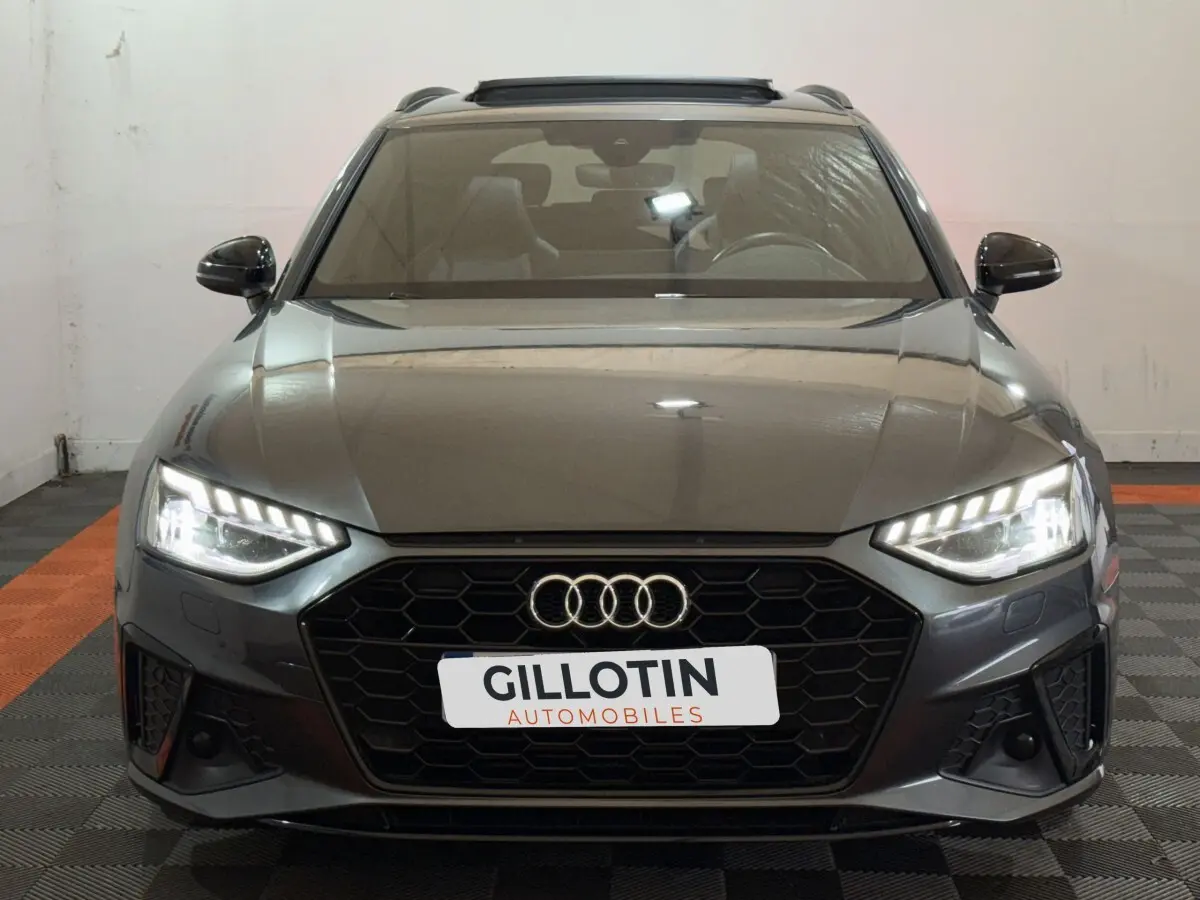 Vue frontale d'une Audi A4 35 TFSI S Edition gris foncé avec phares LED allumés et calandre hexagonale noire.