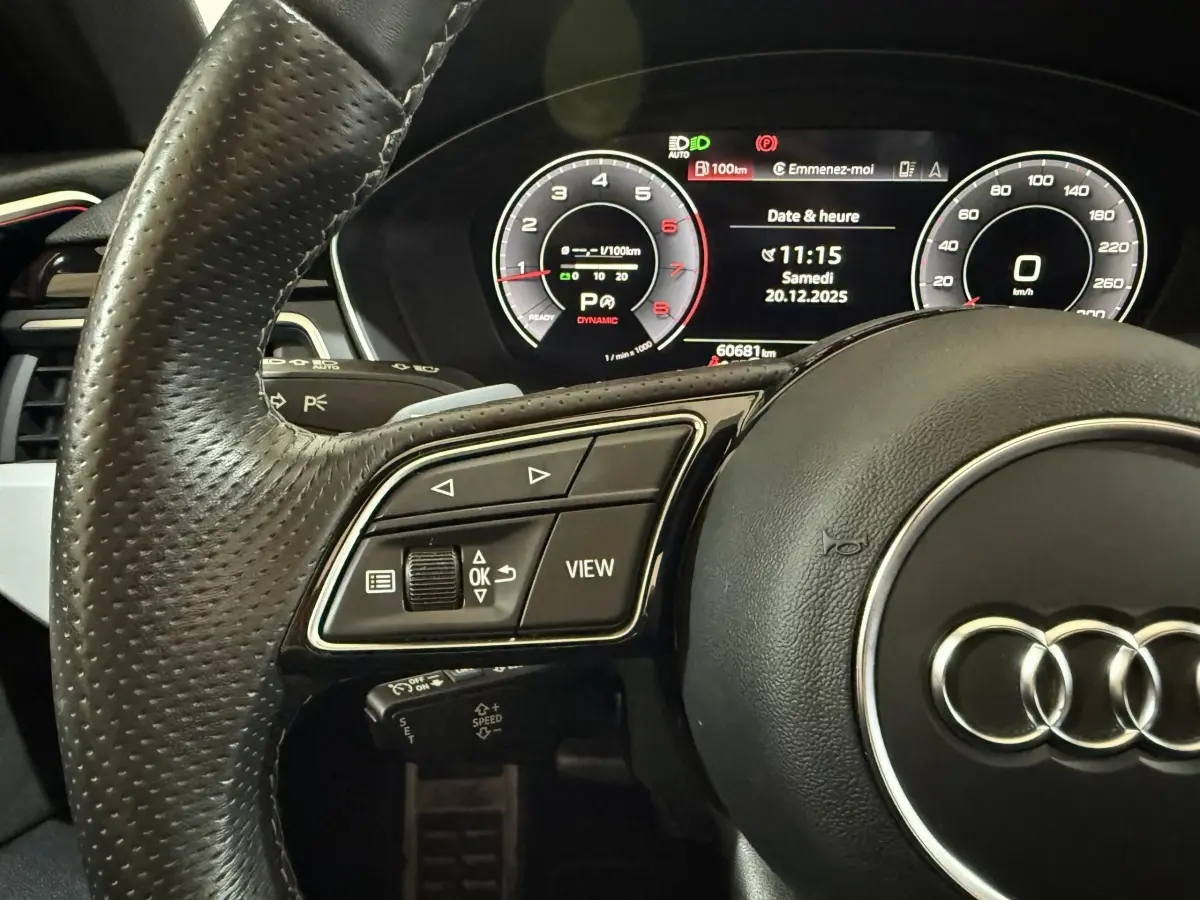 Vue rapprochée du volant cuir et du tableau de bord numérique d'une Audi A4 gris foncé, affichage multifonctions allumé.