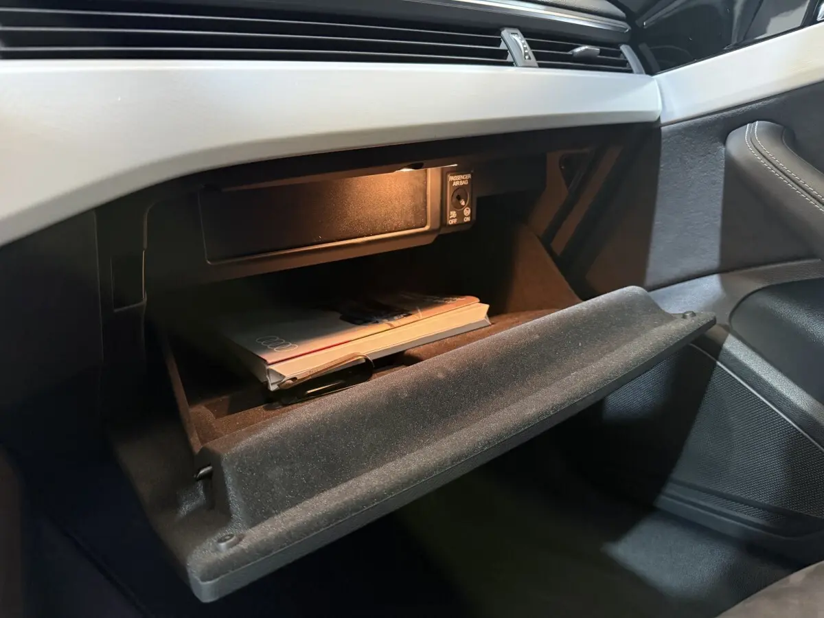 Vue intérieure côté passager de la boîte à gants ouverte avec manuel Audi sur tableau de bord gris clair.