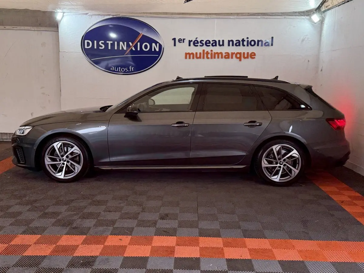 Profil droit d'une Audi A4 35 TFSI S Edition gris foncé en version break, stationnée en intérieur sur sol damier noir et orange.