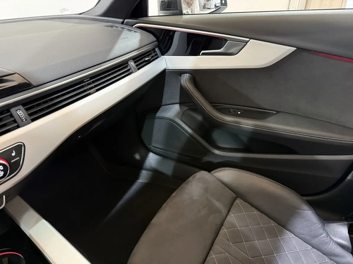 Vue intérieure côté passager de l'Audi A4 gris foncé, mettant en valeur la porte et le siège en cuir avec surpiqûres.