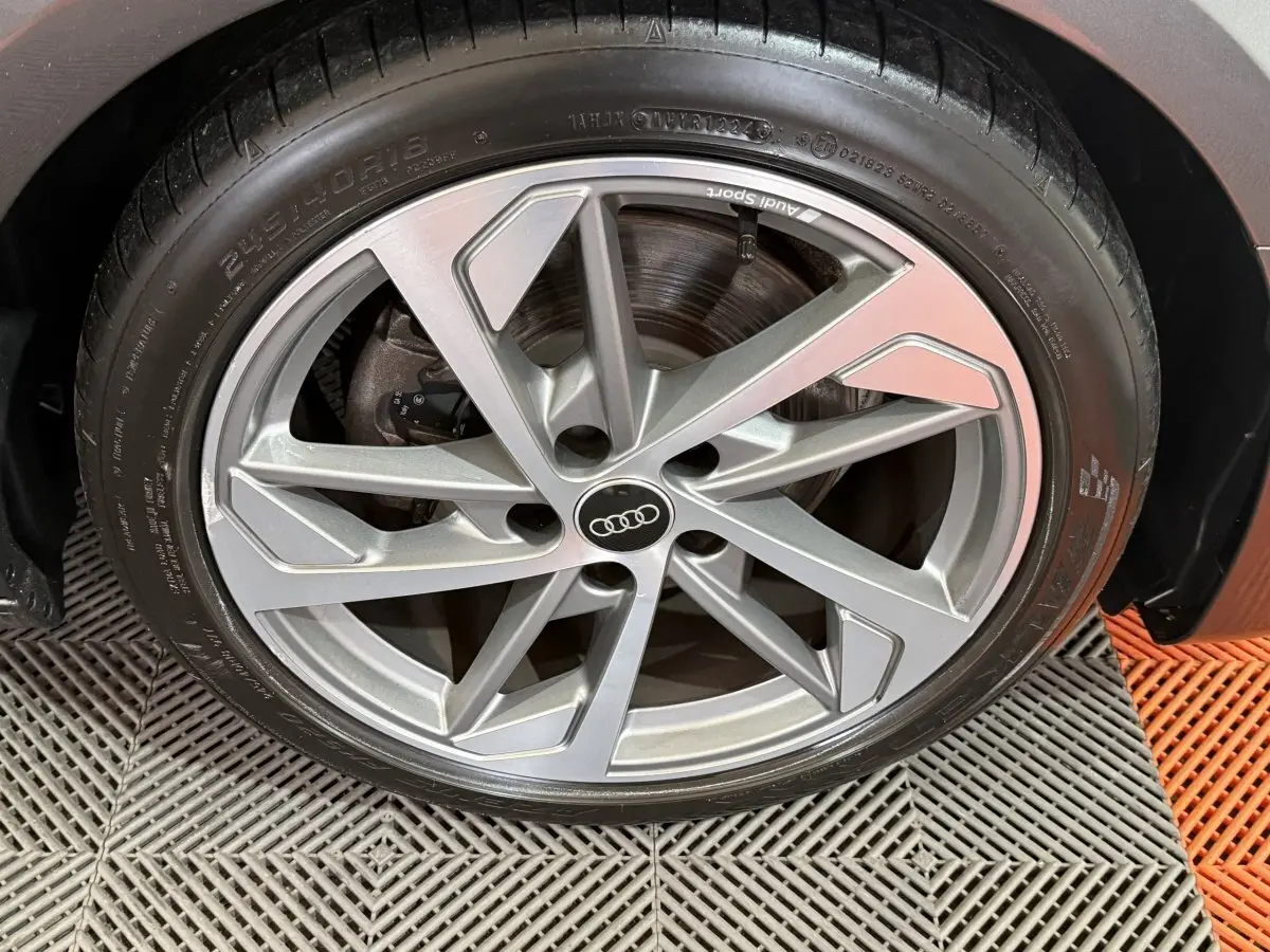 Gros plan sur la jante en alliage argentée Audi Sport d'une Audi A4 gris foncé, roue avant droite visible.