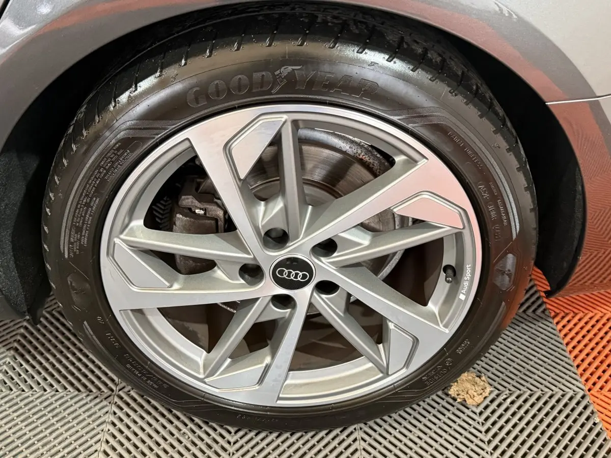 Gros plan sur la roue avant droite d’une Audi A4 gris foncé, jante alliage Audi Sport et pneu Goodyear.
