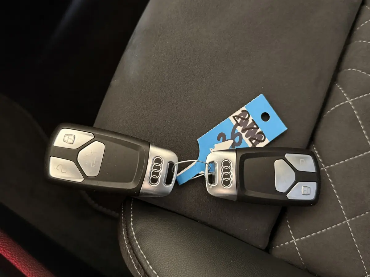 Gros plan sur deux clés Audi noires avec logo argent posées sur un siège en cuir noir et tissu gris.